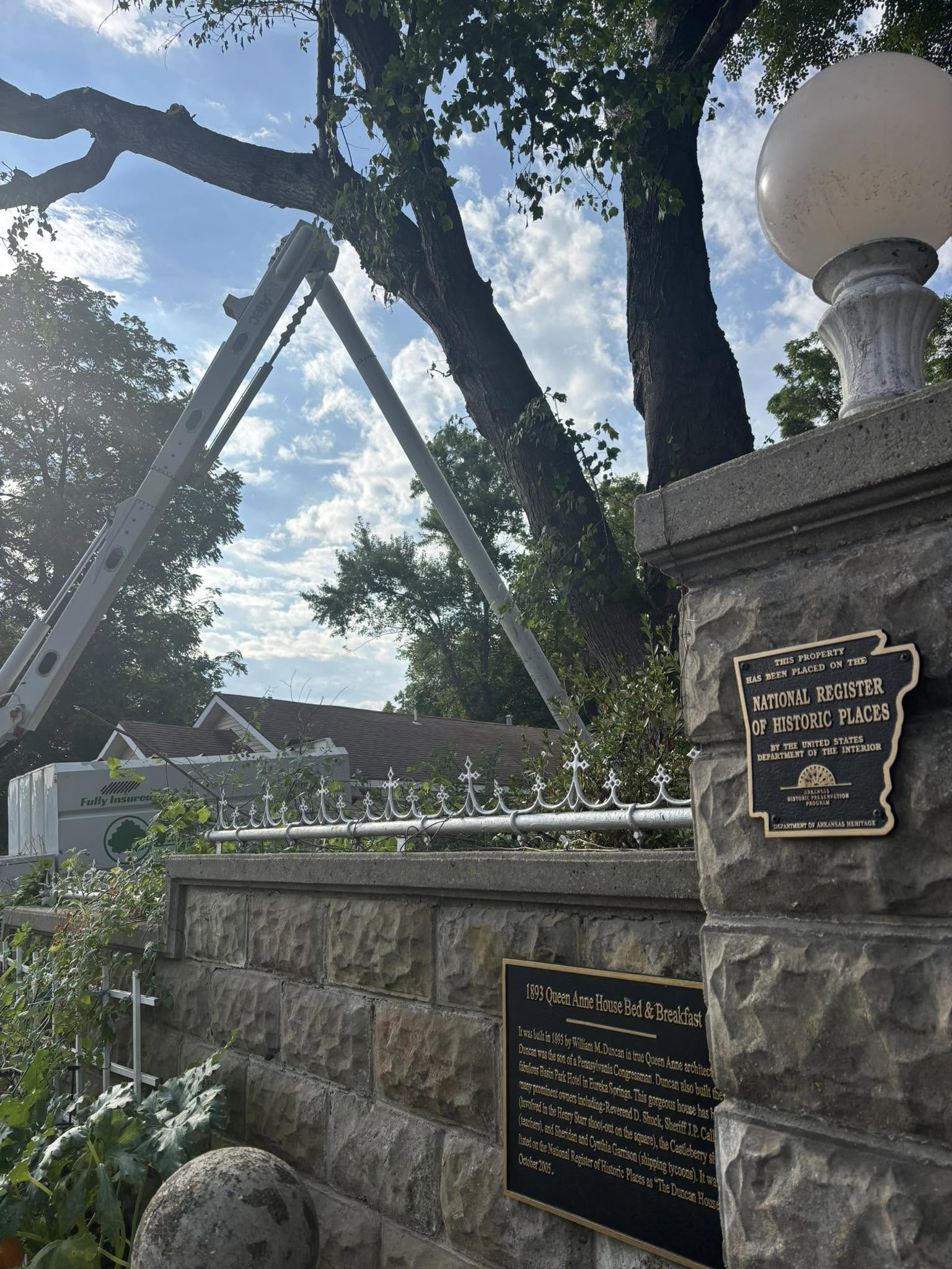 Stone memorial with plaques under trees and a crane against a bright sky