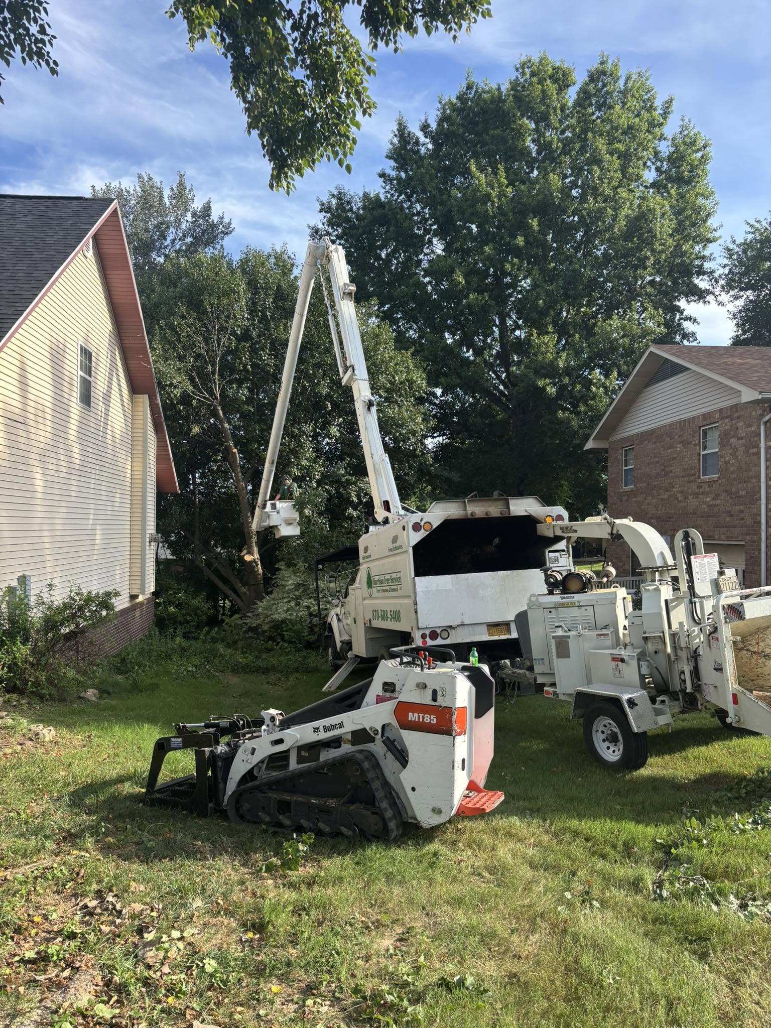 Two white utility lifts in a yard, one raised beside a house and trees on a sunny day.