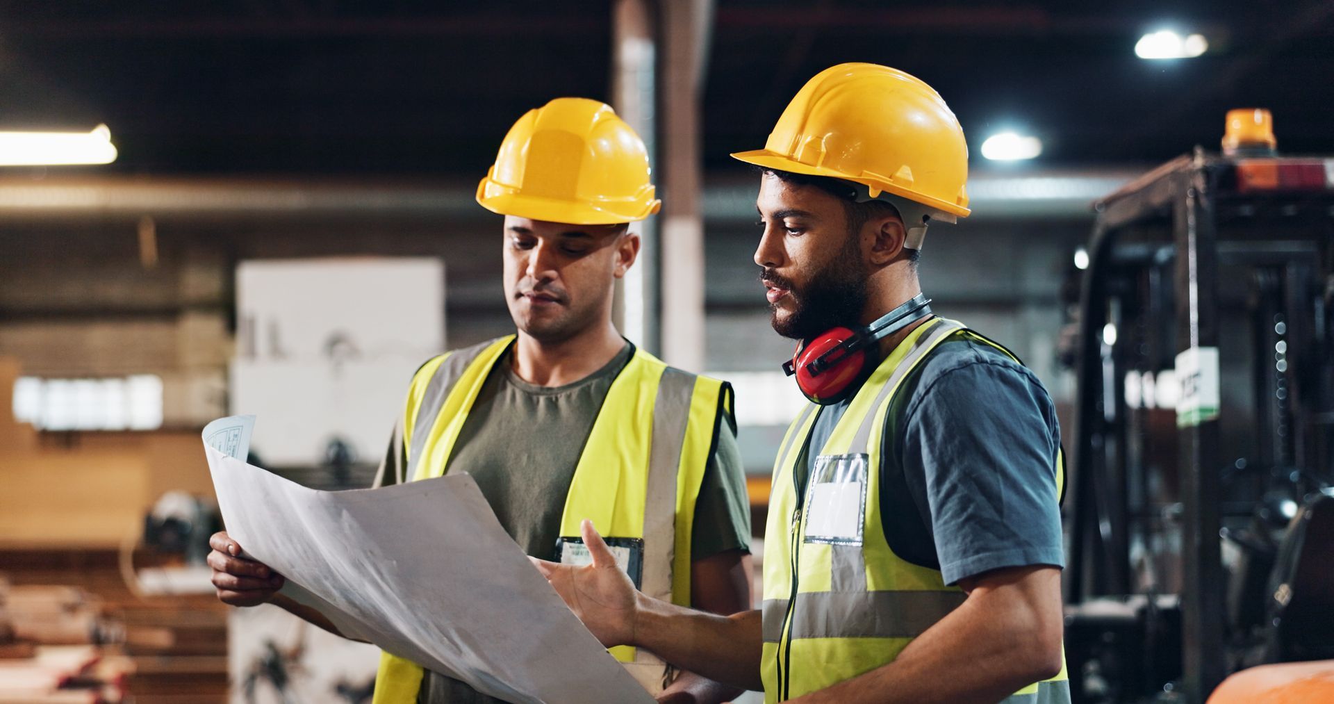 Industrial tools supplier workers reviewing blueprint at construction site wearing safety helmets.