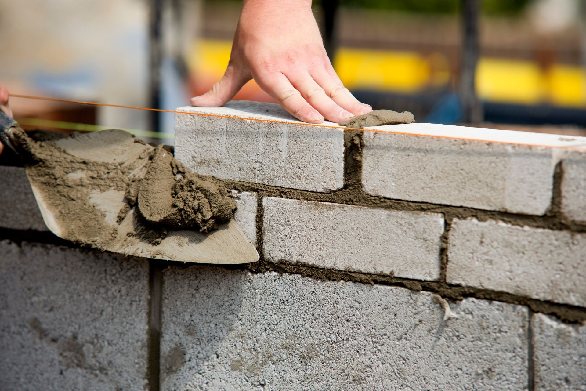 A worker lays bricks for a structure at a building site using tools and materials for masonry work.