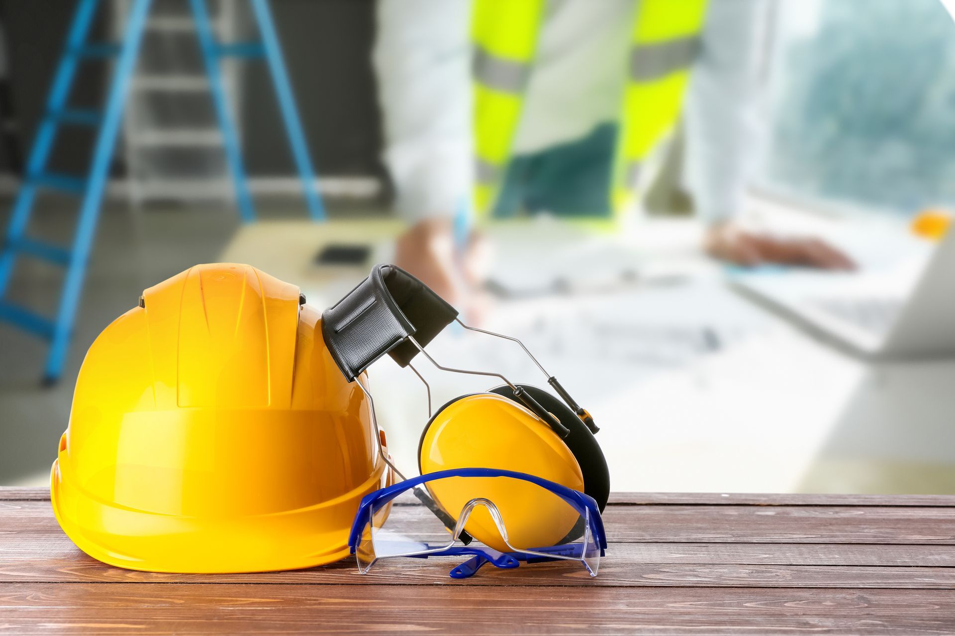 Safety hardhat and protective earmuffs with glasses on wooden table.
