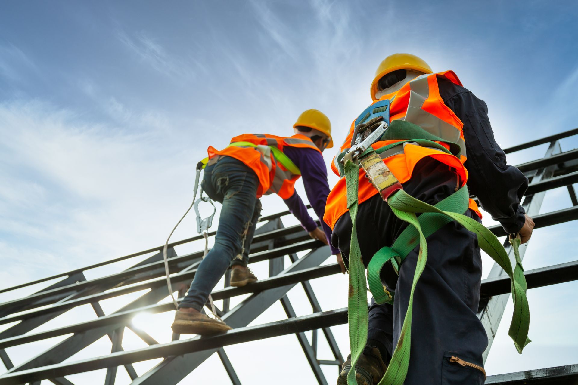 Workers climbing a metal structure while wearing safety harnesses and high visibility gear.