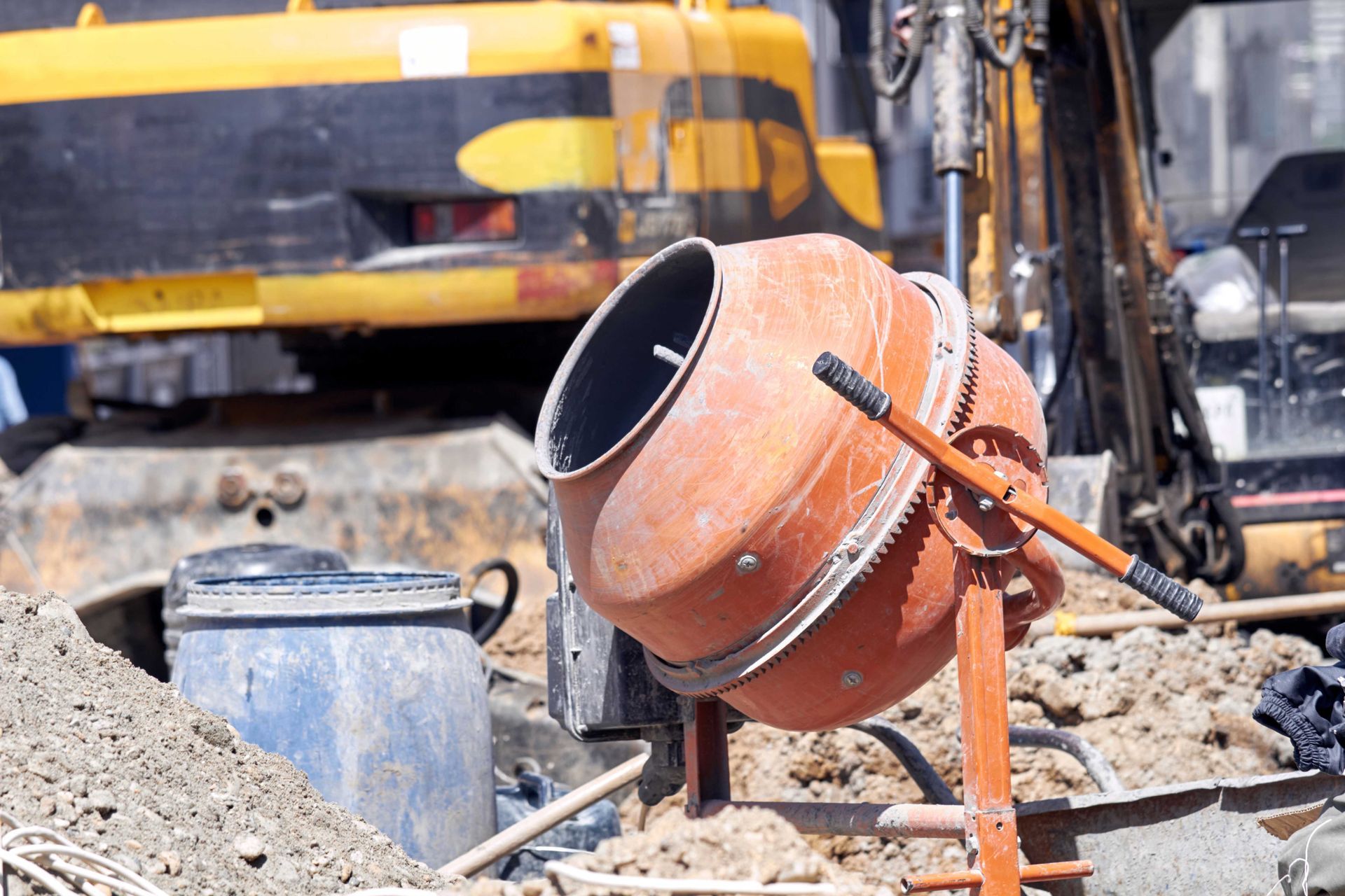 Orange cement mixer at a construction site with dirt piles and heavy machinery in the background