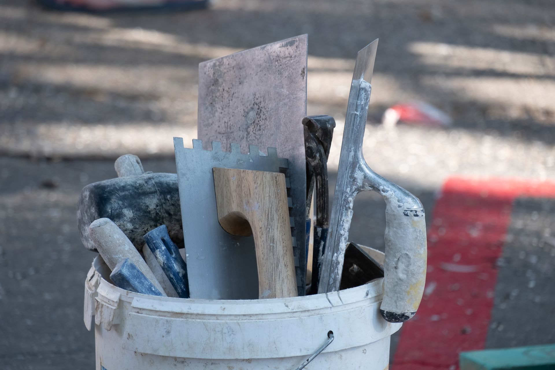 White bucket filled with garden hand tools and trowels on pavement