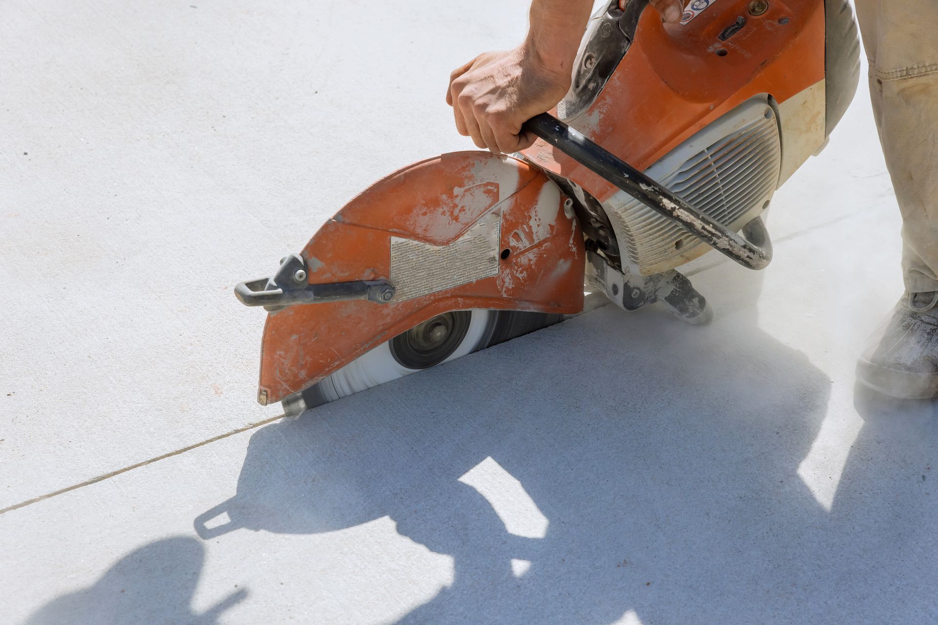 Close-up of a worker using a diamond blade saw to cut concrete on a concrete sidewalk.