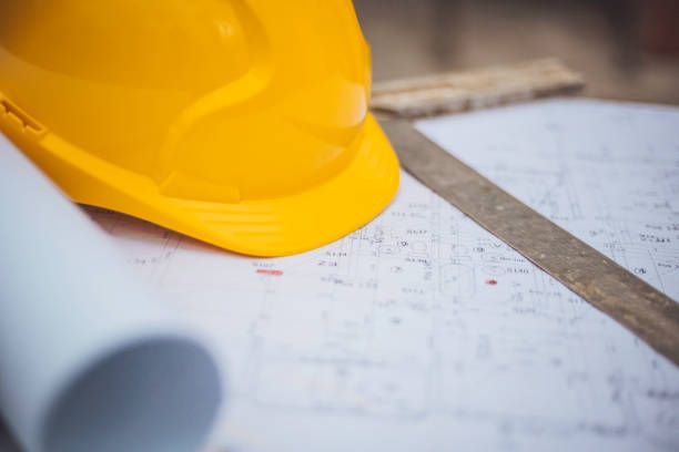 Yellow construction hard hat on architectural blueprints with ruler for building planning safety pro.
