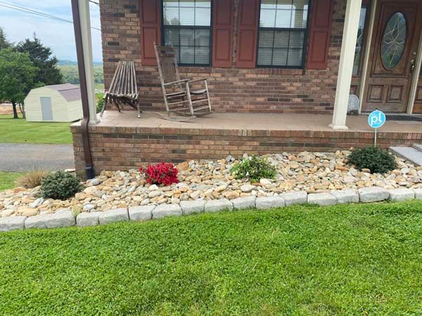 Front porch with wicker chairs and a rock garden bordered by white stones and red flowers.