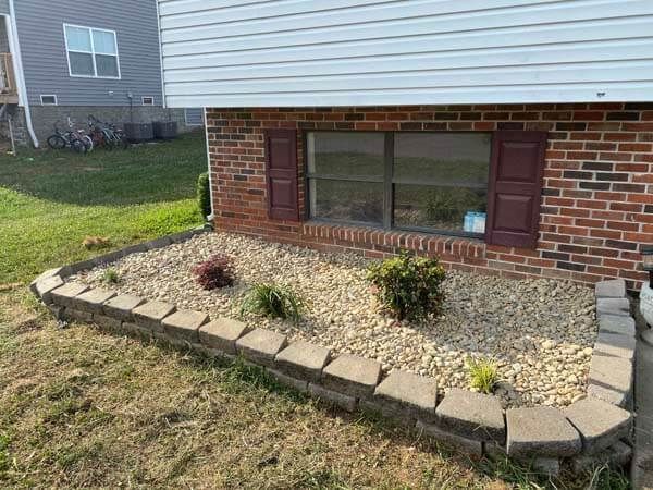 Front yard flower bed with stone border and mulch beneath a house window