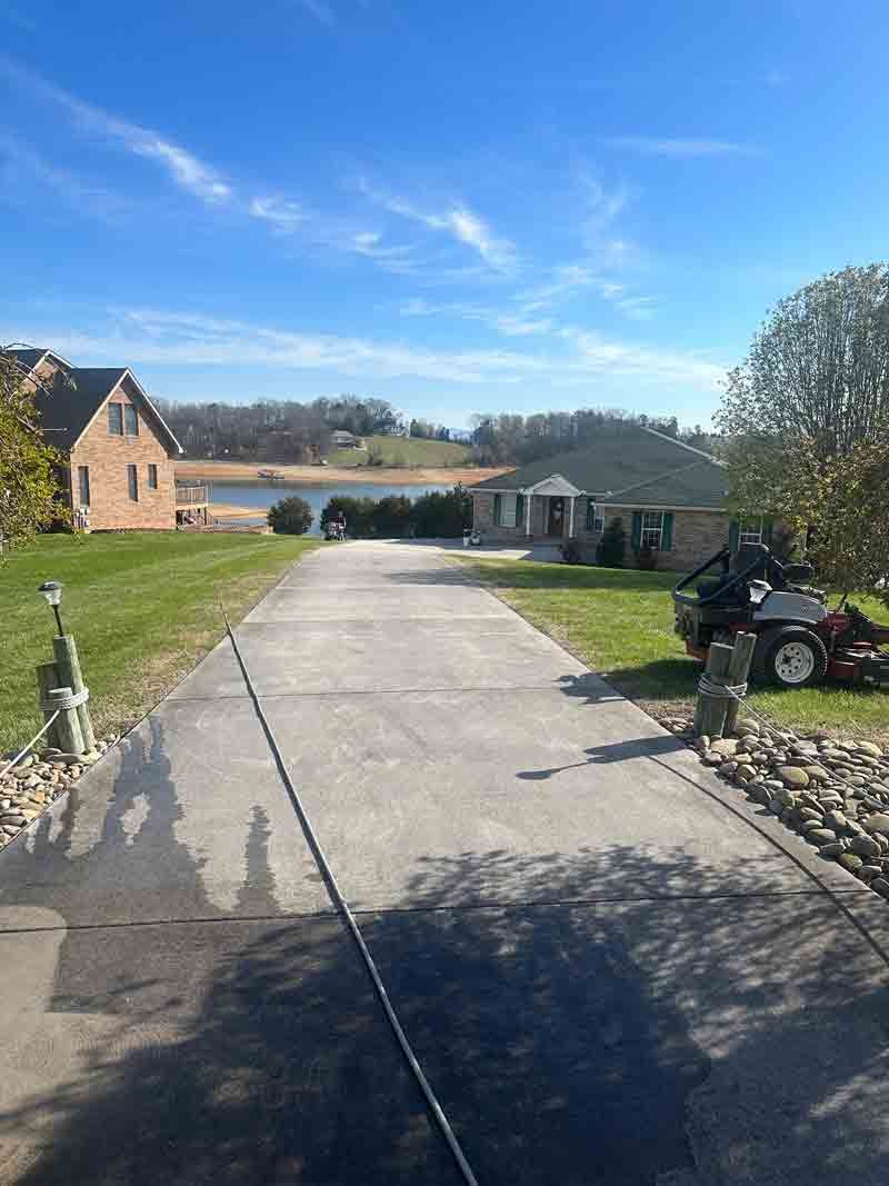 Long driveway to a house by a river, with a parked vehicle and clear blue sky.