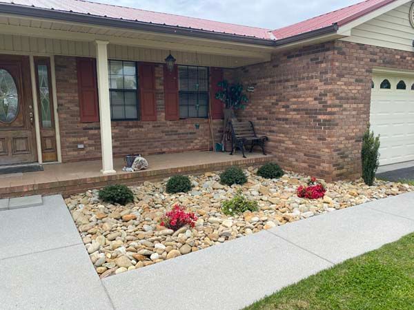 Front yard with brick house, white garage, and rock landscaping with red flowers and shrubs