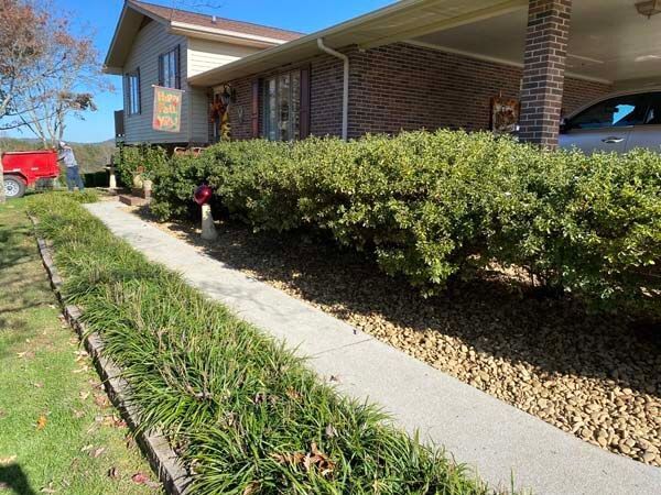 Brick house with red roof, front walkway, and neatly trimmed shrubs along a sunny yard