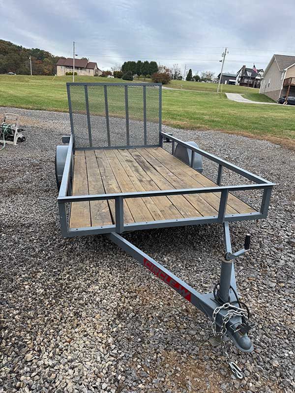 Small metal utility trailer with a wooden floor and mesh ramp on gravel in a residential yard