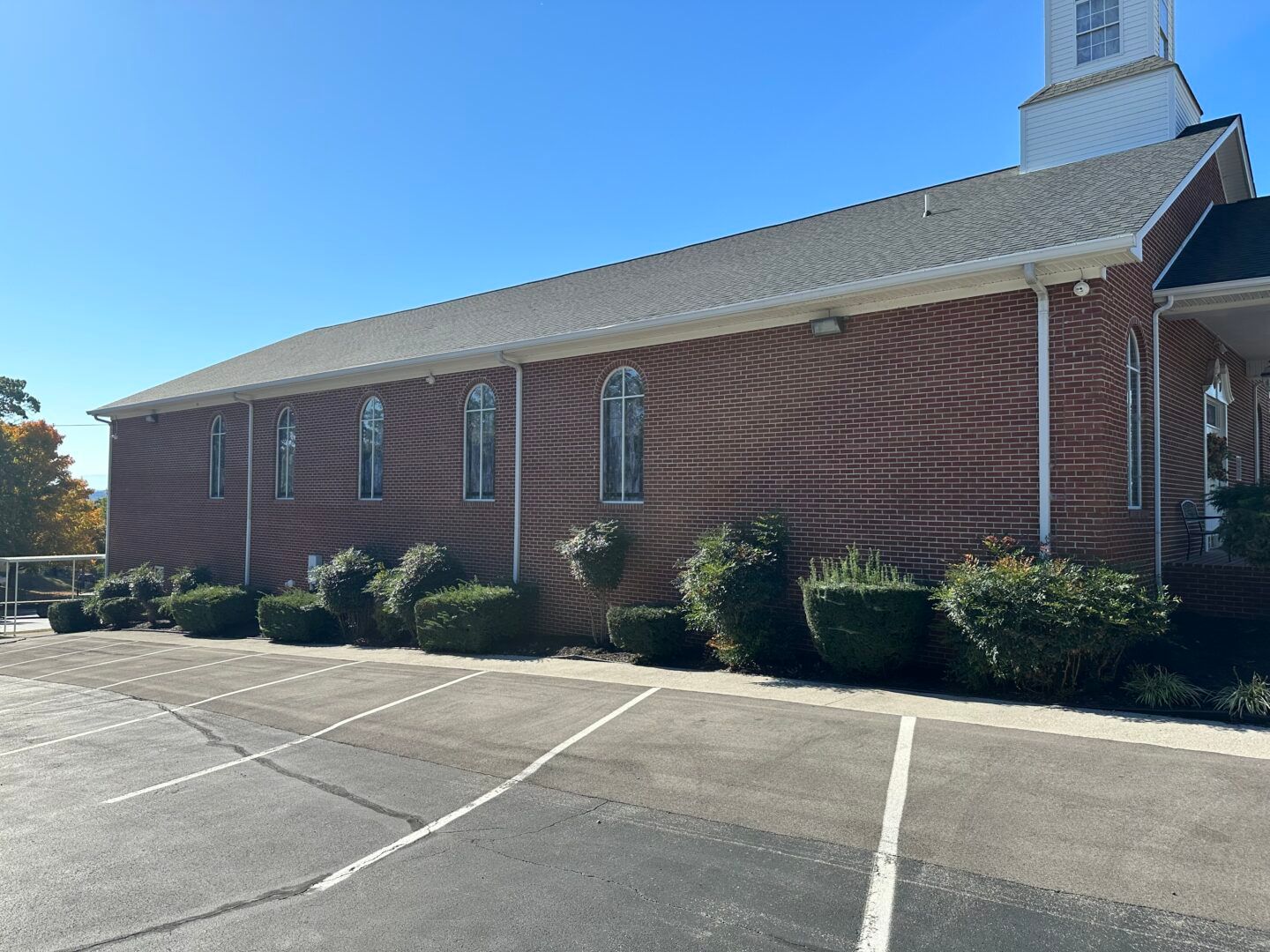 Brick church with white steeple beside an empty parking lot on a sunny day