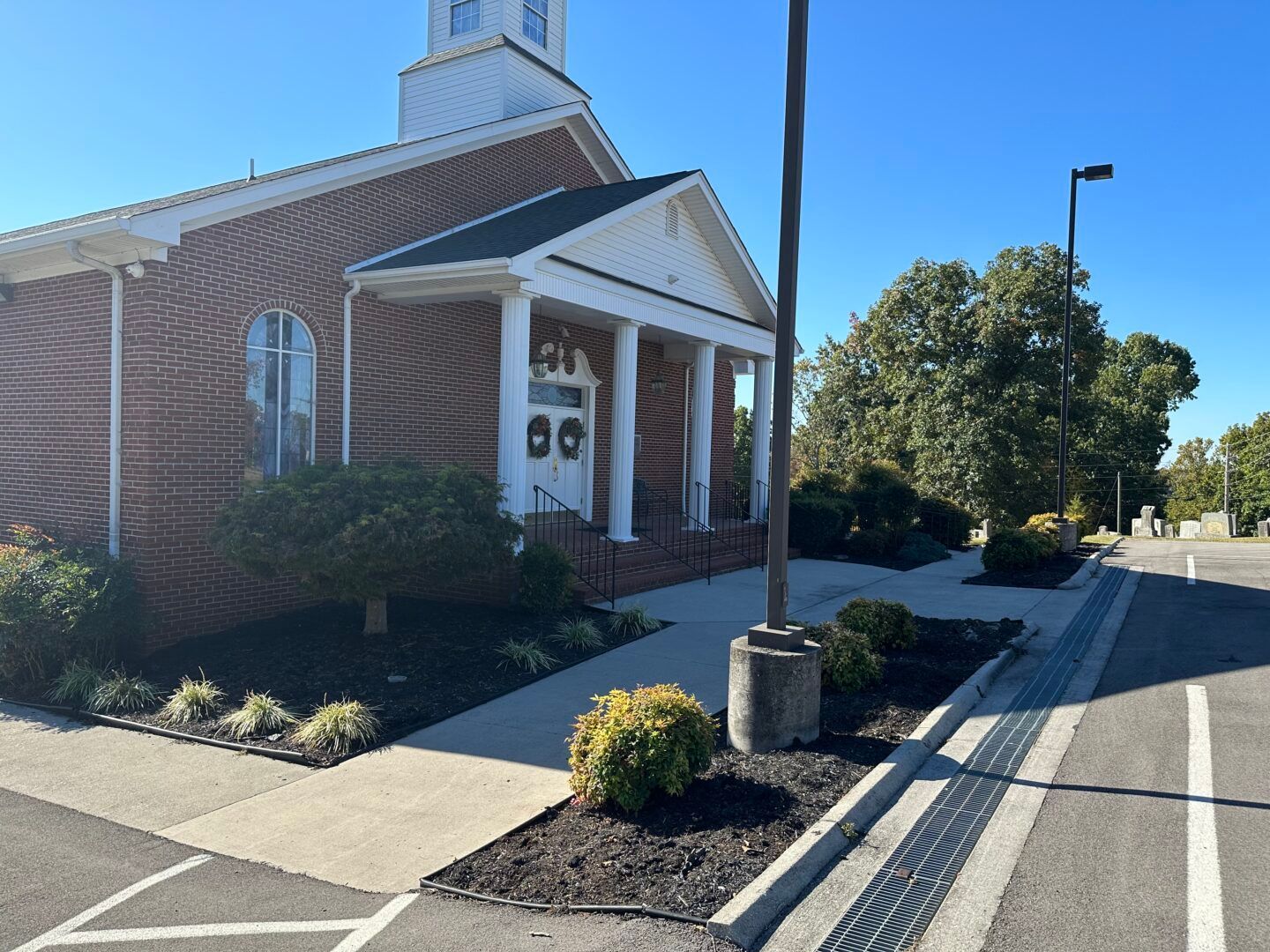 Brick church entrance with white columns, flower beds, and a clear blue sky on a sunny day