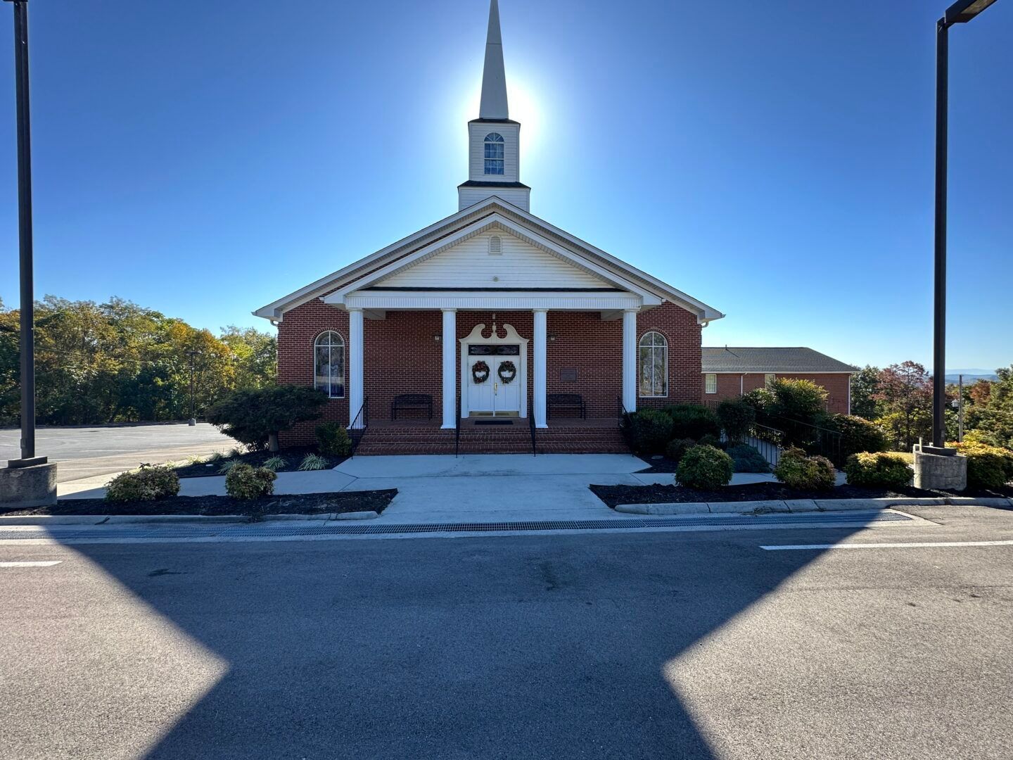 Small brick church with white steeple and entrance, centered under a bright blue sky.