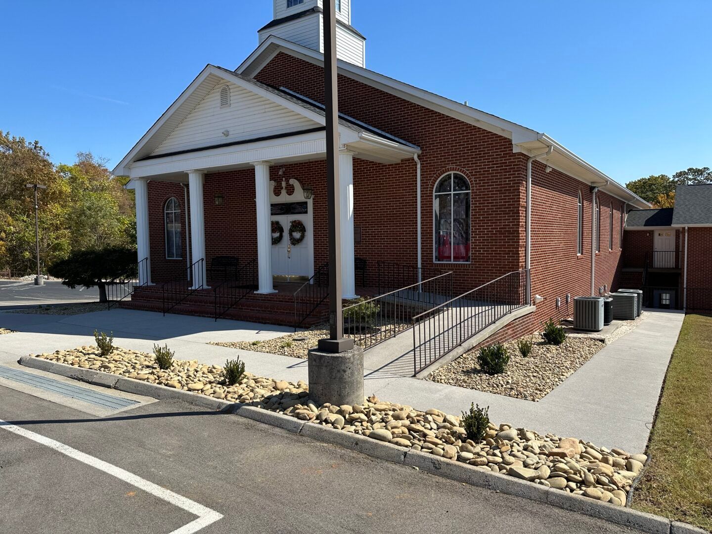 Red brick church with white columns and a wheelchair ramp beside a paved parking lot