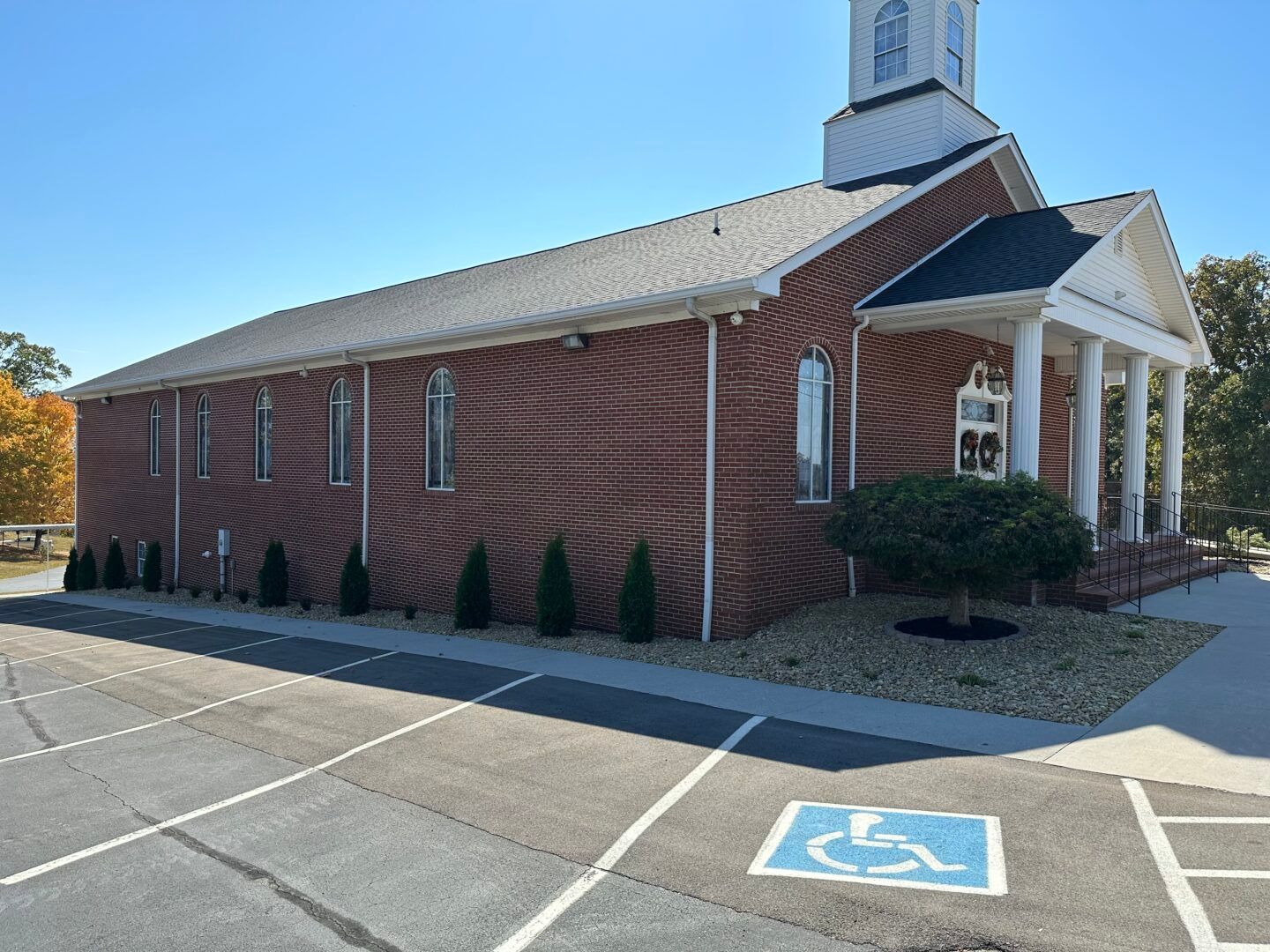Small red brick church with white columns and steeple beside an accessible parking space.