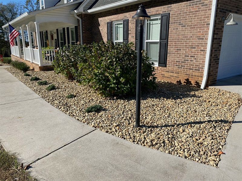 Brick house with front porch, black shutters, and gravel landscaping beside a sidewalk