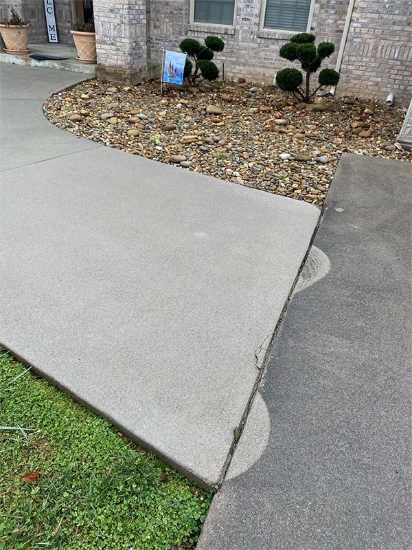 Concrete walkway with a cracked edge beside a landscaped gravel bed and house exterior.