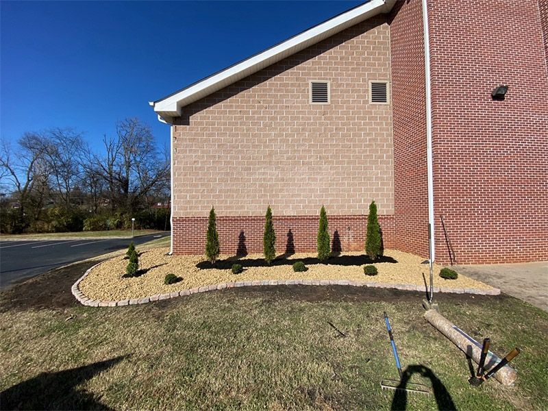 Brick building corner with young shrubs in a mulched bed beside a parking lot