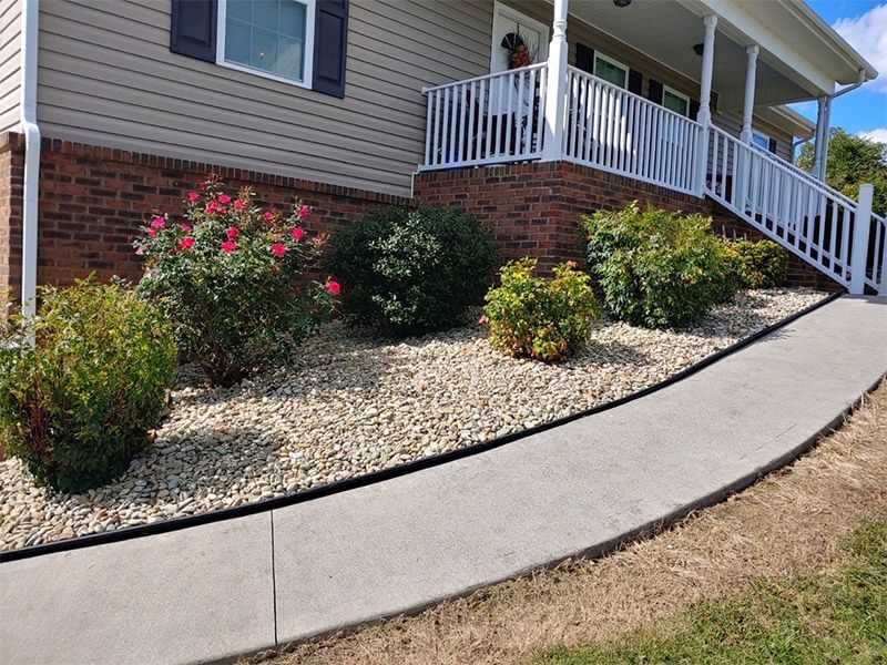 Landscaped house front with shrubs, rose bushes, and a curved concrete sidewalk beside a porch