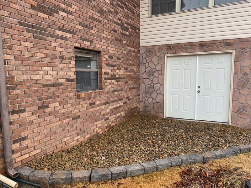 Brick townhouse exterior with a window, double white doors, and a stone-bordered leaf-covered entryway