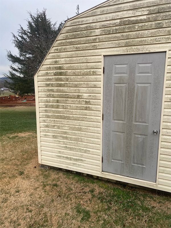 Small beige shed with a gray door on a grassy yard, with a tree in the background.
