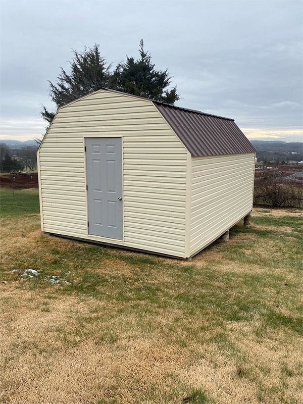 Small cream-and-brown shed with a gray door on a grassy field under a cloudy sky