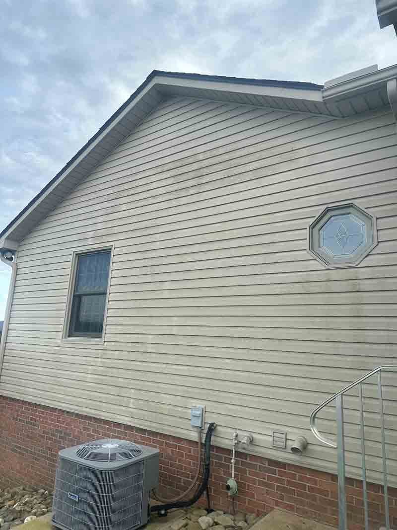 Side view of a beige house with brick foundation, a small octagonal window, and an HVAC unit outside