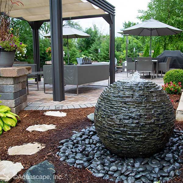 Modern backyard patio with stone water feature, pergola, outdoor seating, and umbrellas