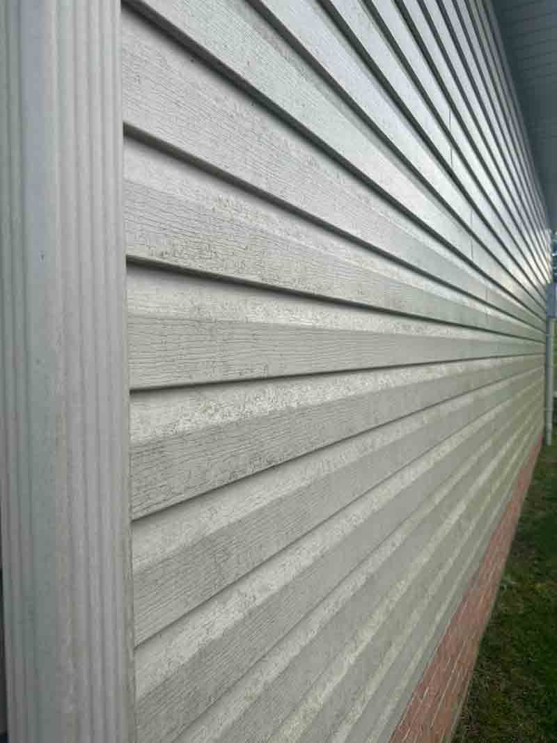 Close-up of beige vinyl siding on a house exterior with a grassy yard beside it.