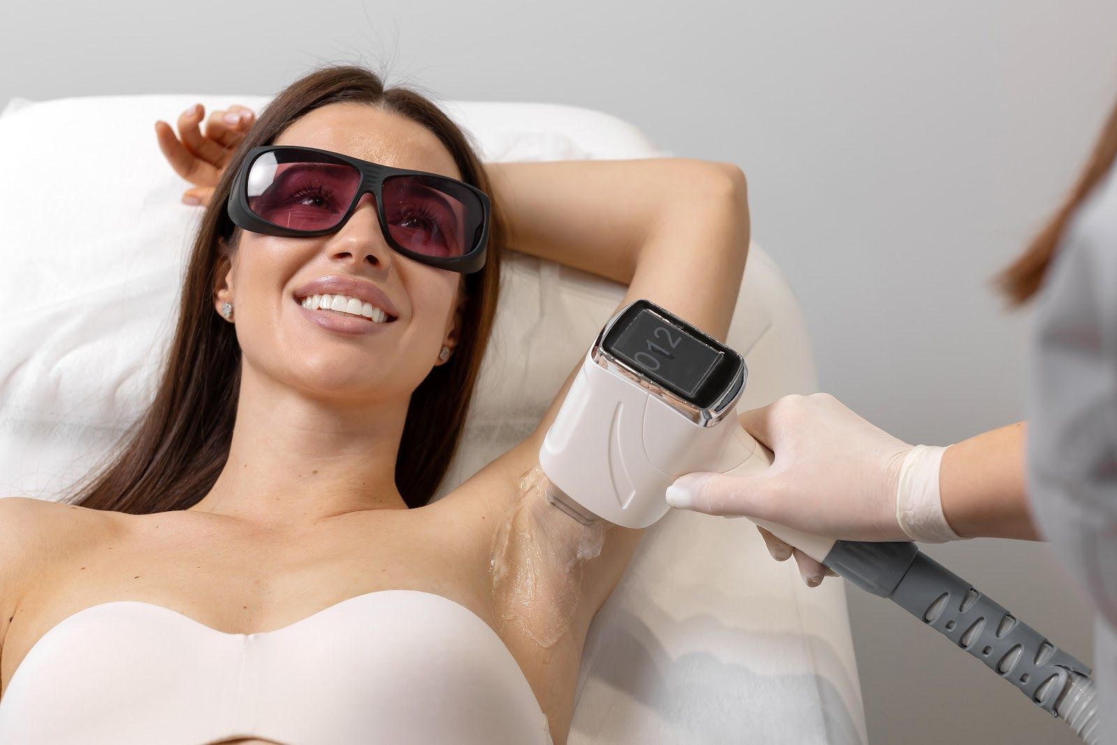 Woman wearing goggles receives a laser treatment on her underarm in a spa clinic