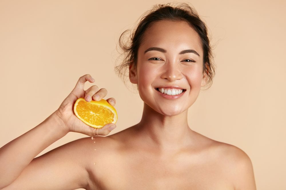 Smiling woman holding a sliced orange against a beige background