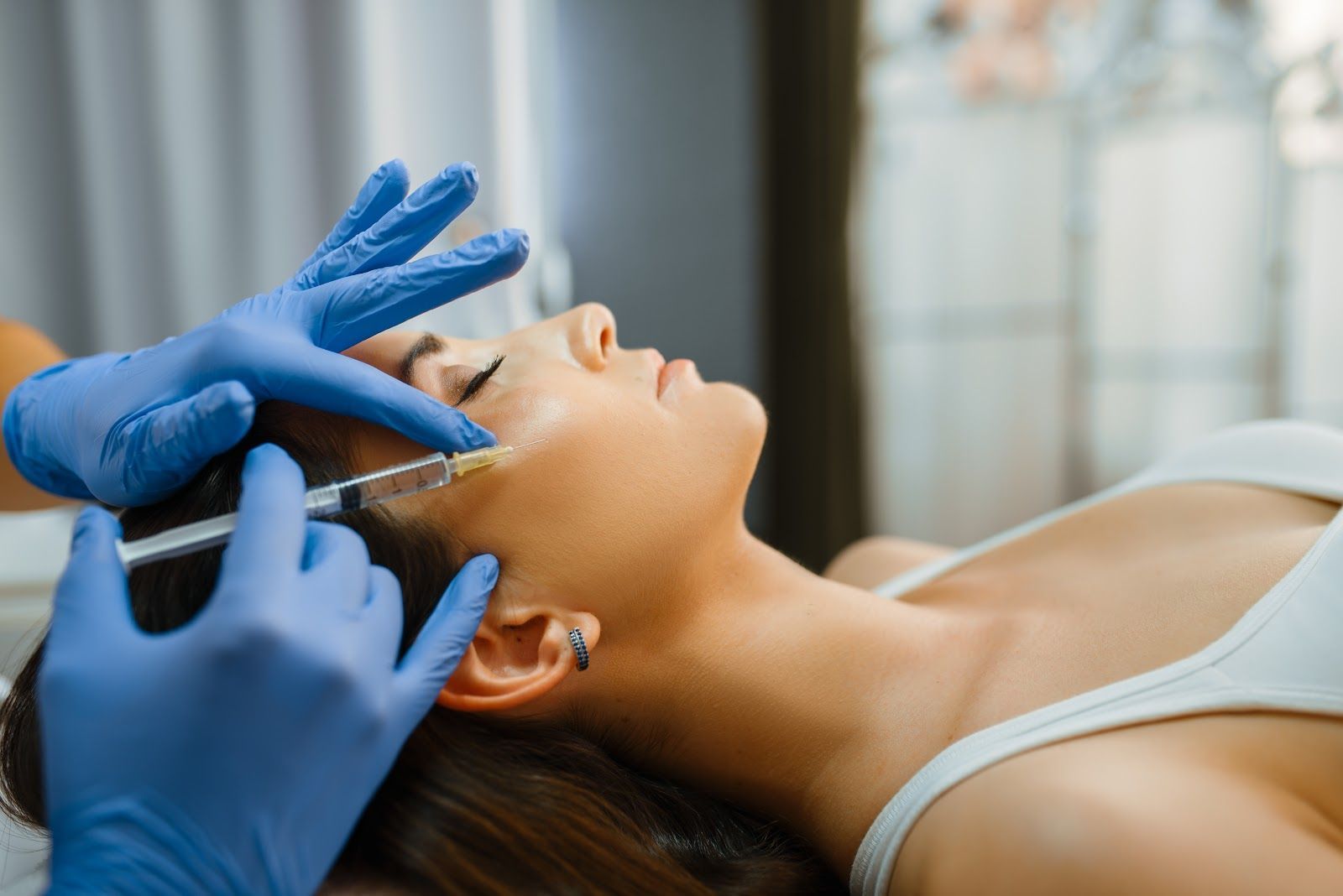 Gloved practitioner applying facial treatment to a reclining patient in a spa setting