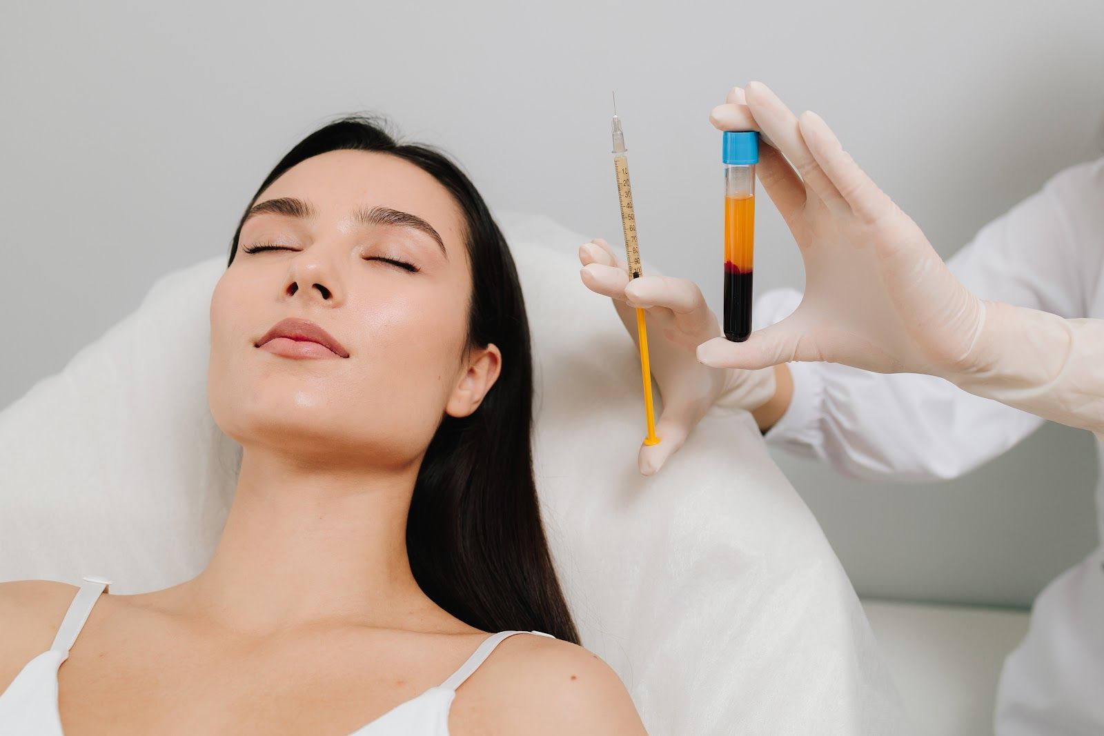 Woman lying with eyes closed while a gloved hand holds a syringe and vial beside her face