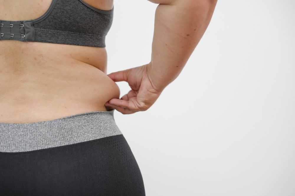 Person pinching side waist fat in gray sportswear against a plain white background