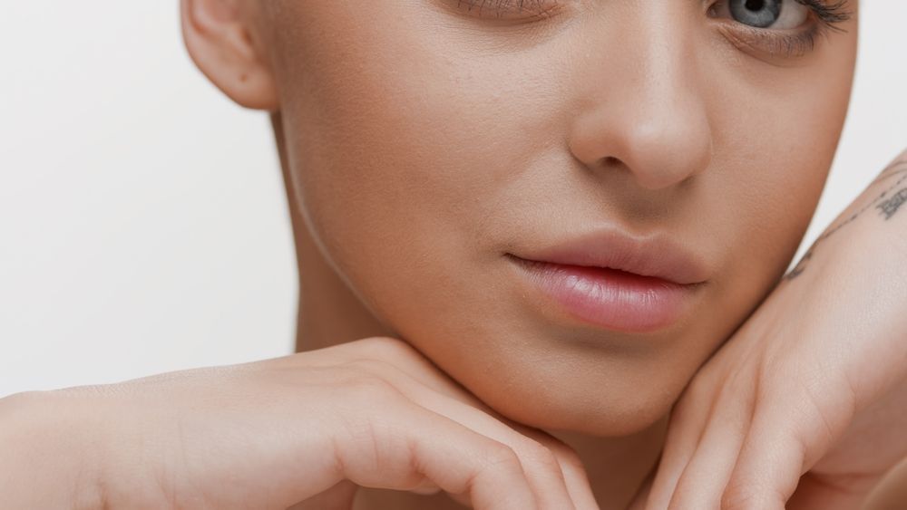 Close-up of a person resting their chin on their hands, with a neutral expression against a plain background