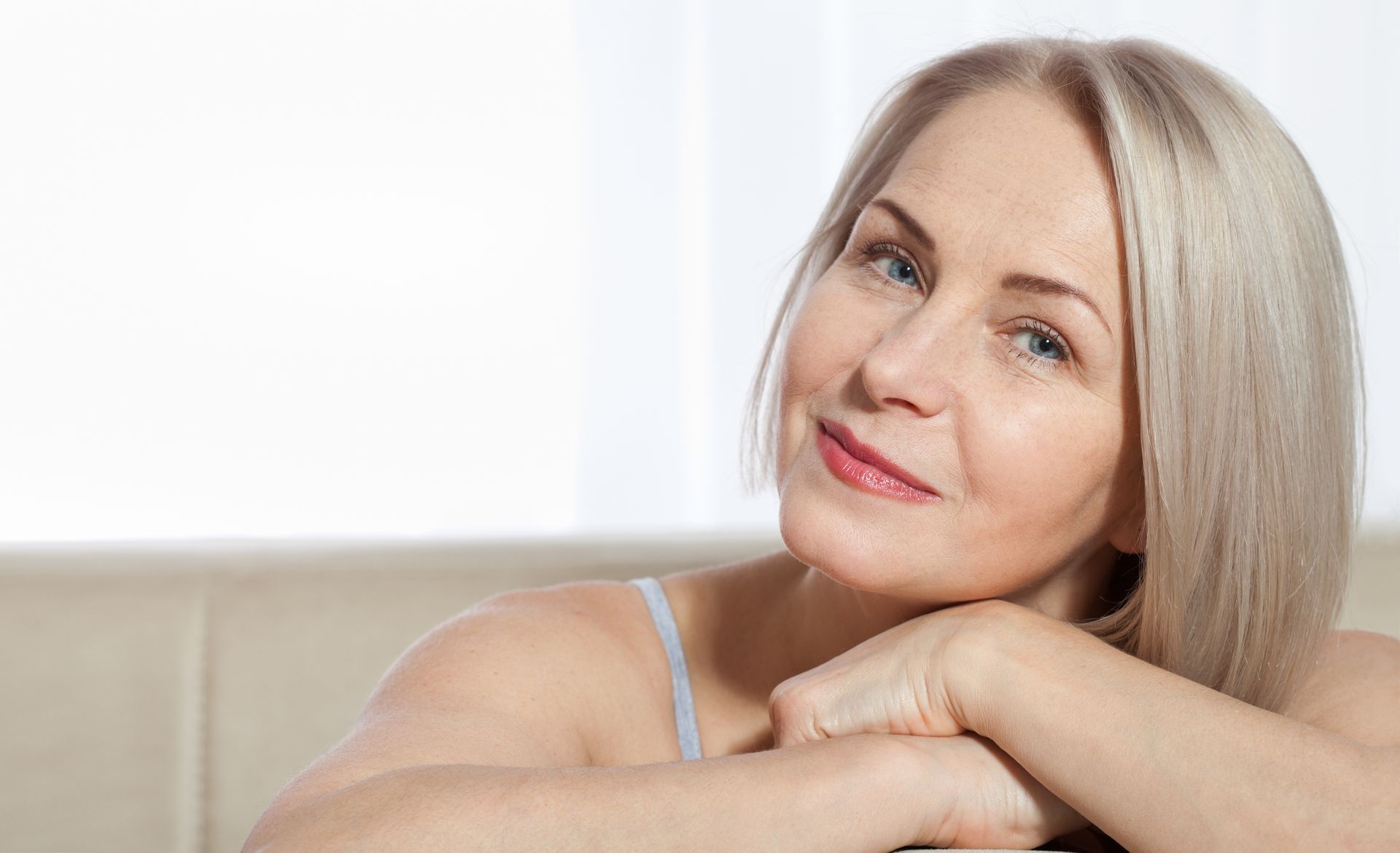 A woman is smiling and touching her face with her hand.