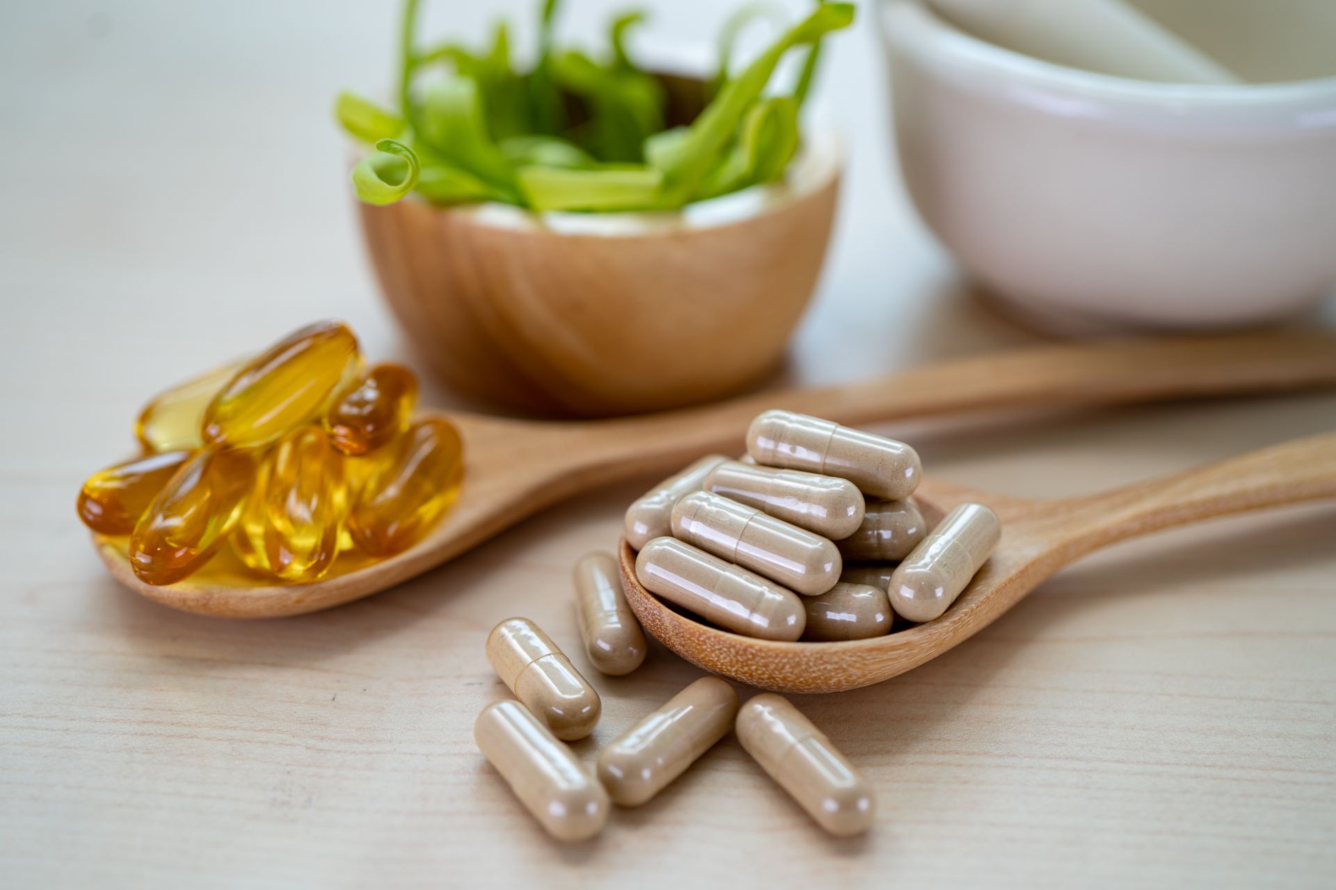 A wooden spoon filled with pills next to a bowl of pills and a mortar and pestle.