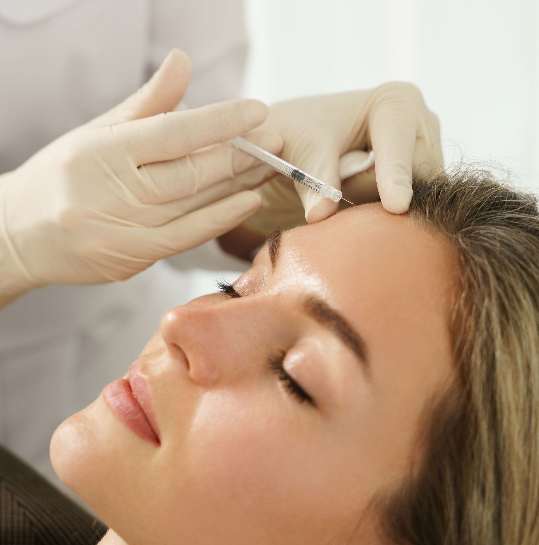 A woman is getting a botox injection in her forehead.