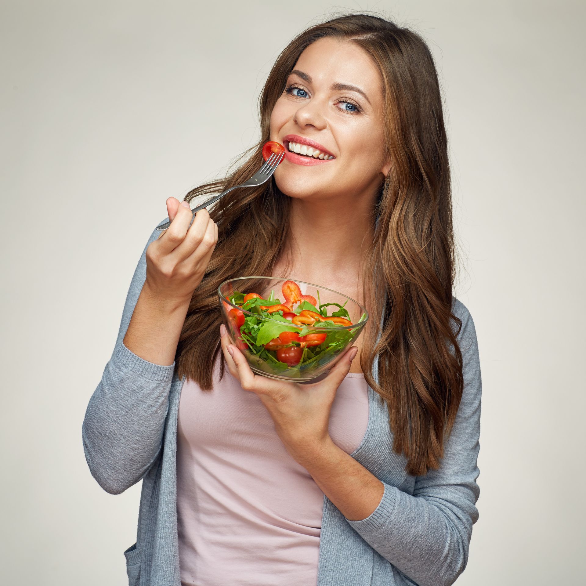 A woman is eating a salad with a fork from a bowl.