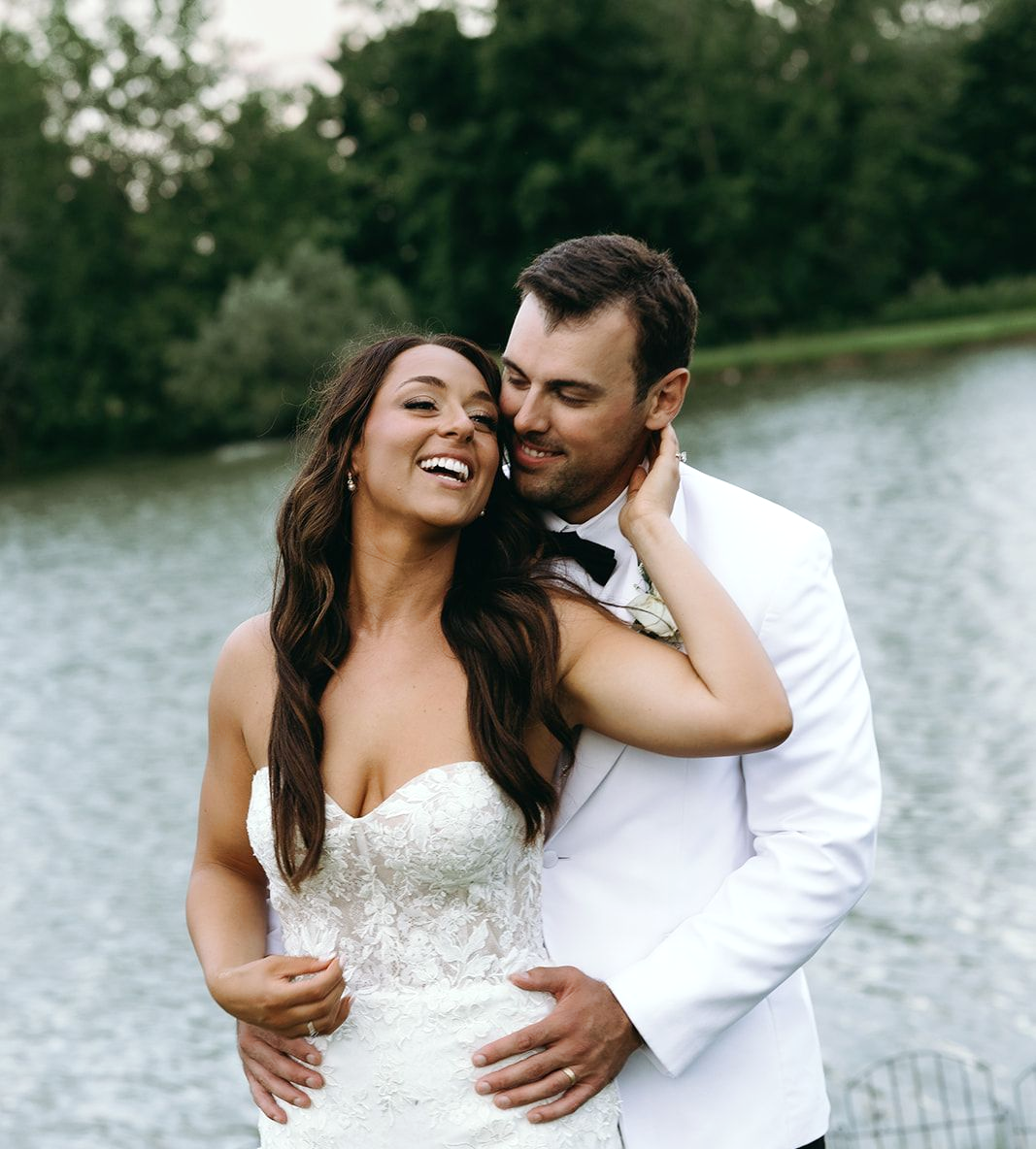 The bride and groom are posing for a picture with their wedding party in front of a lake.