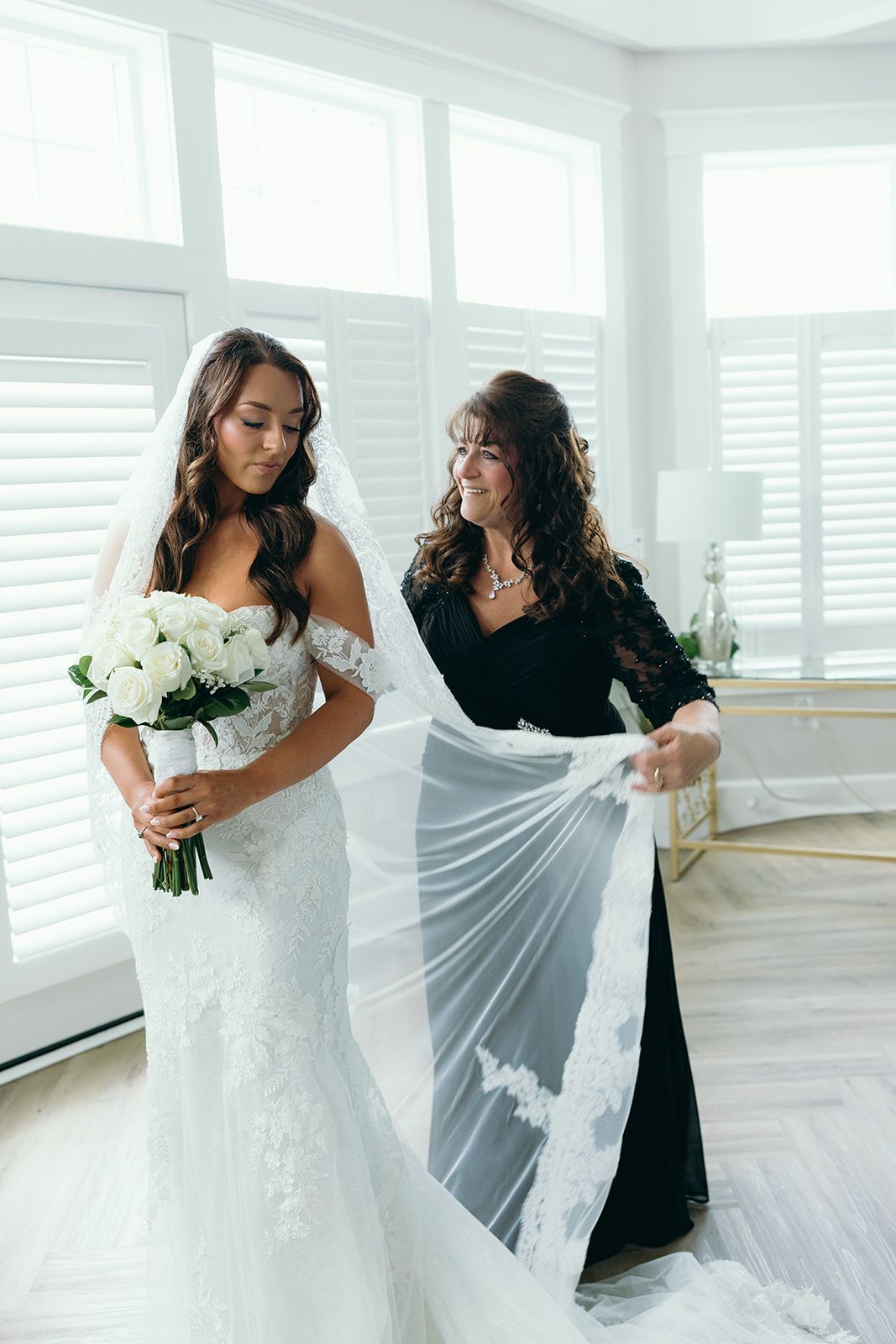 A woman is helping a bride get ready for her wedding in front of a mirror.