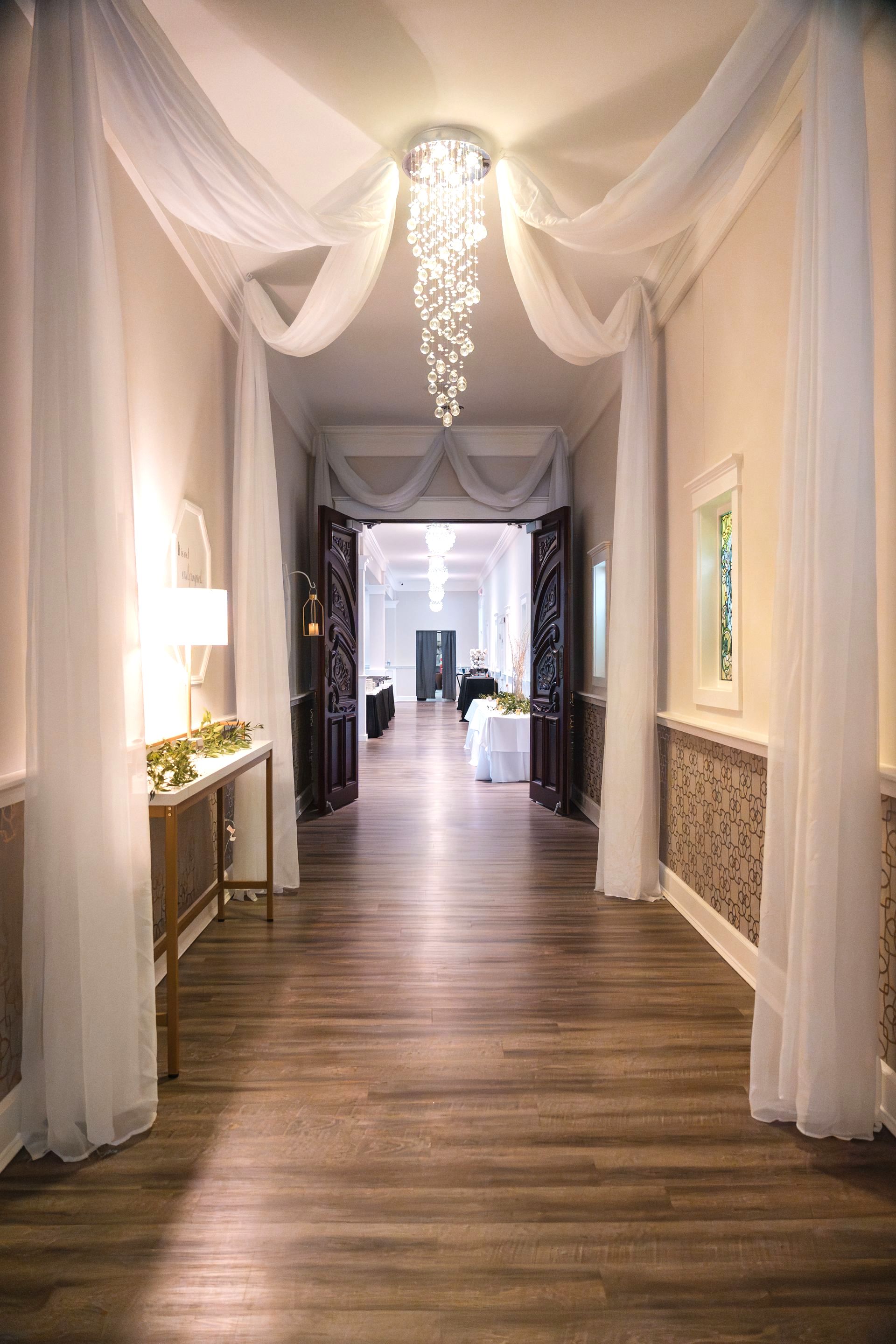 A long hallway with wooden floors and a chandelier hanging from the ceiling.