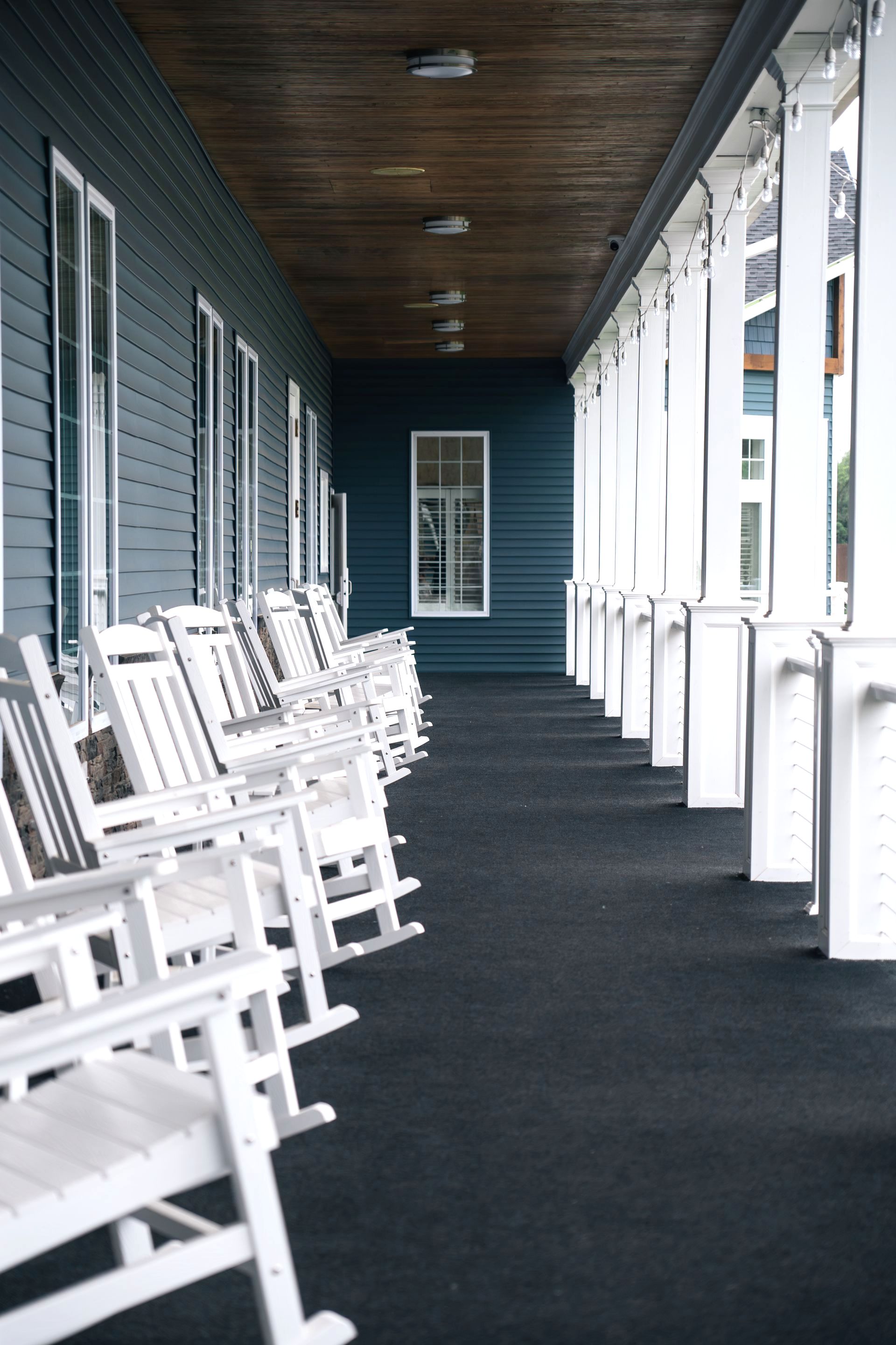 A row of white rocking chairs are lined up on a porch.