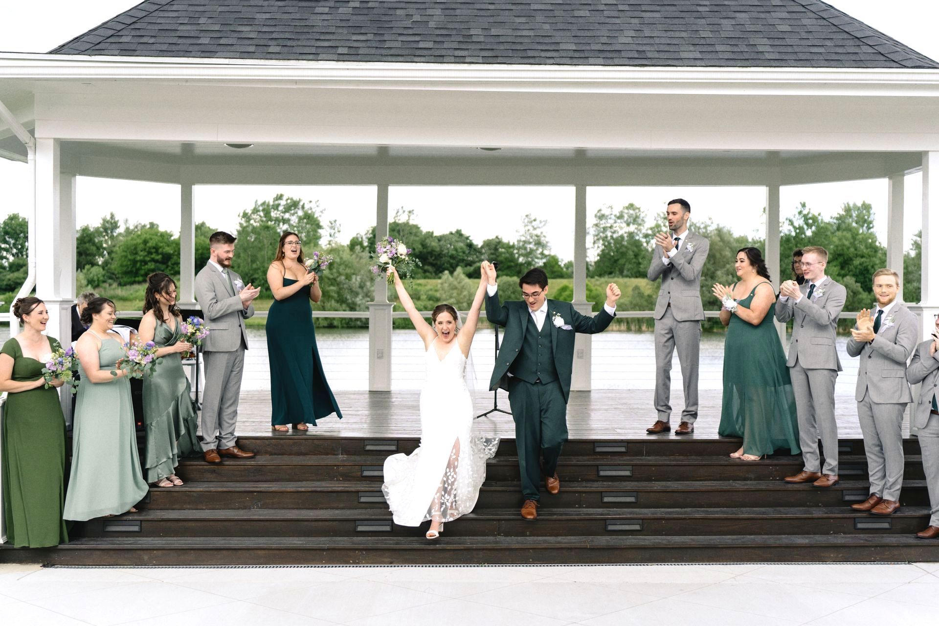 A bride and groom are posing for a picture with their wedding party in front of a gazebo.