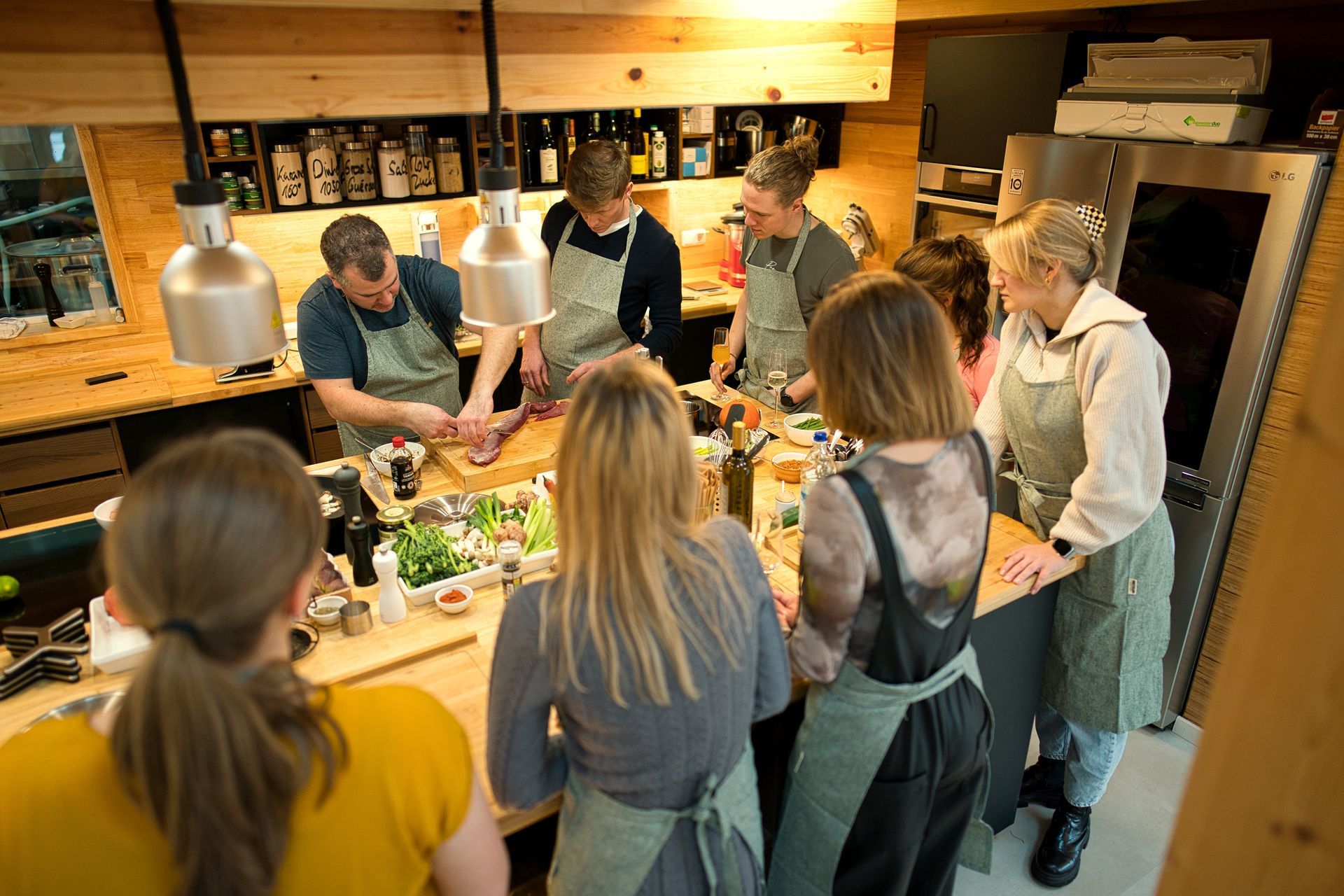 Menschen bereiten in einer Küche Essen zu. Ein Mann schneidet Fleisch, andere beobachten und bereiten es vor.