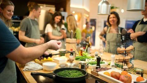 Menschen kochen in einer Küche, ein Mann kocht in einer Pfanne. Gemüse und Zutaten auf der Theke.
