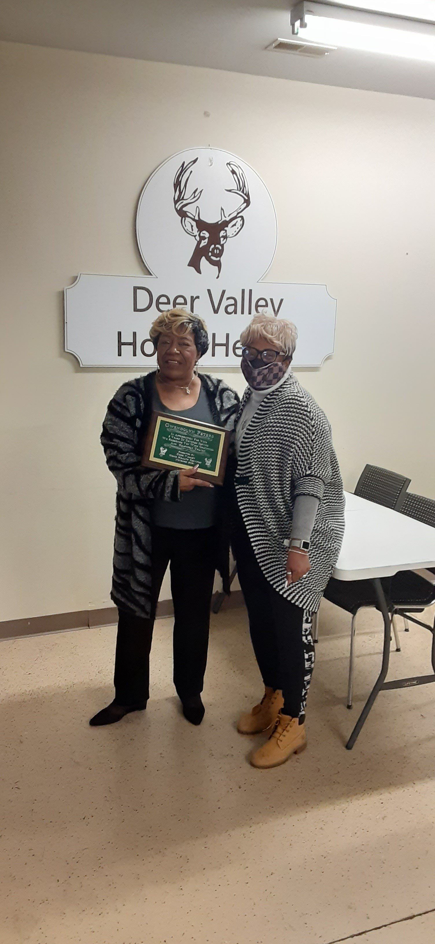 Two women standing in front of a sign for Deer Valley Home Health, one holding a framed award.