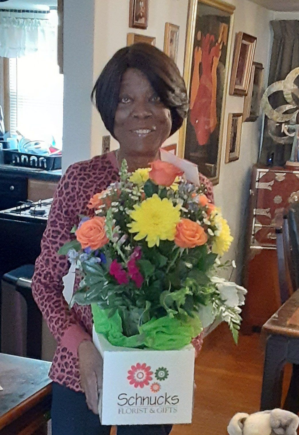 Woman smiles, holding floral arrangement from Schnucks. Orange roses, yellow daisy, green foliage.